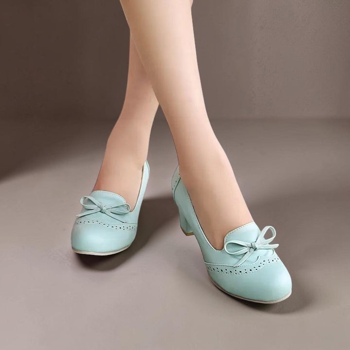 Vivian &amp; Cole Adelaide light blue slip-on pumps with a decorative bow and perforated detailing on a low block heel.