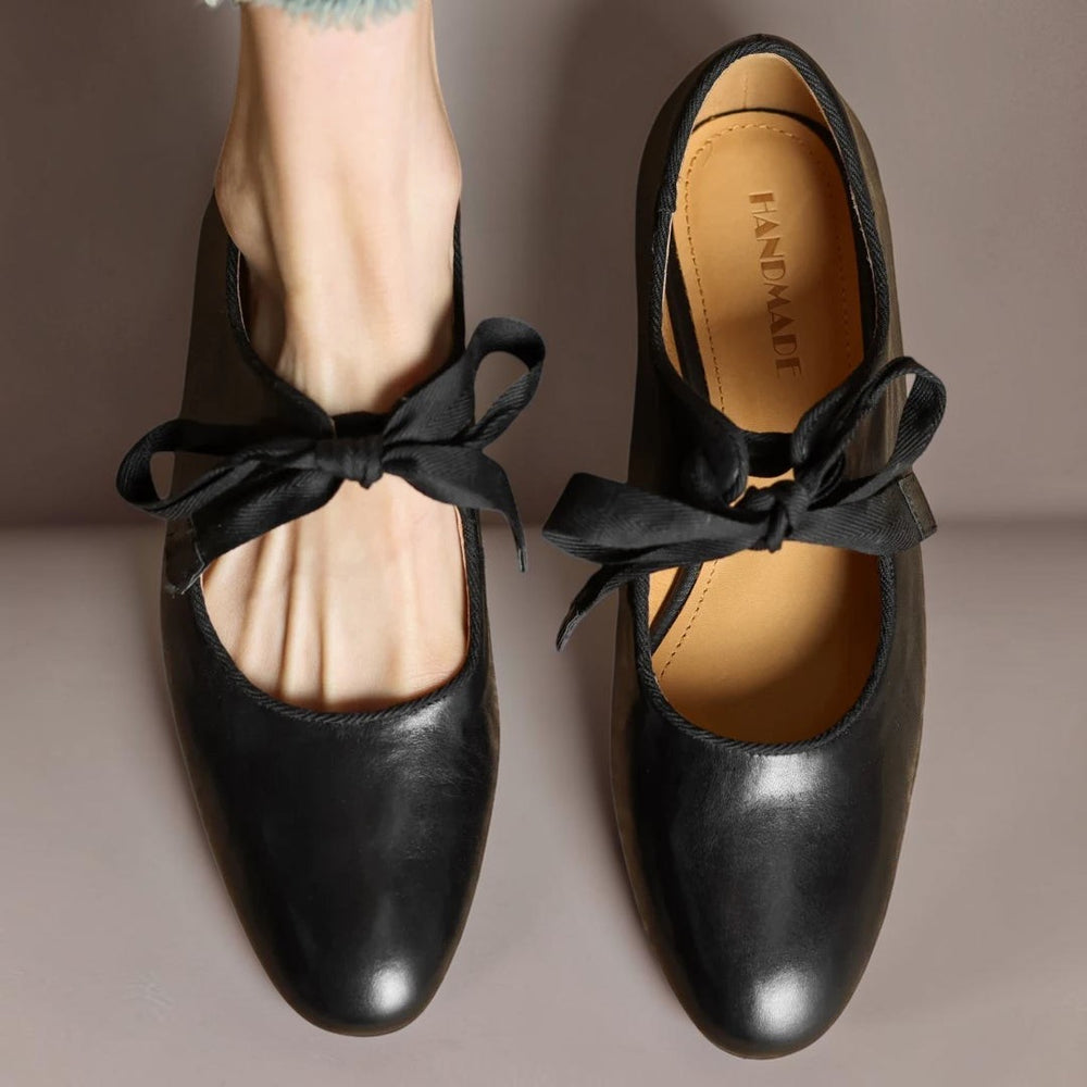 Vivian & Cole black leather Mary Jane flats with a decorative bow detail worn on a foot against a neutral background