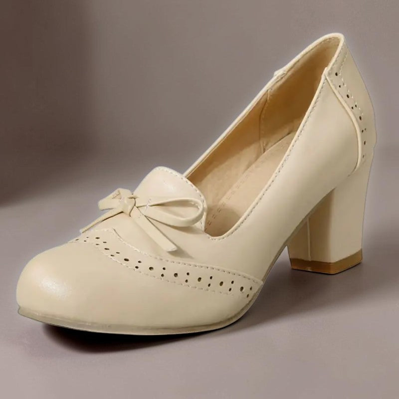 Vivian &amp; Cole Adelaide beige slip-on pumps with a bow detail, block heel, and decorative brogue-style perforations.