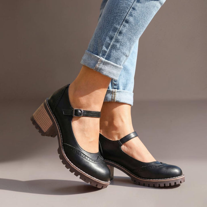Vivian &amp; Cole Marie black T-strap Mary Jane heels with a chunky lug sole, worn with blue jeans on a sunny sidewalk.