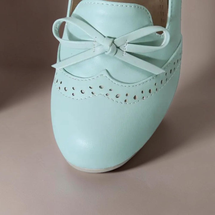 Vivian &amp; Cole Adelaide light blue slip-on pump featuring a decorative bow and delicate brogue-style perforations