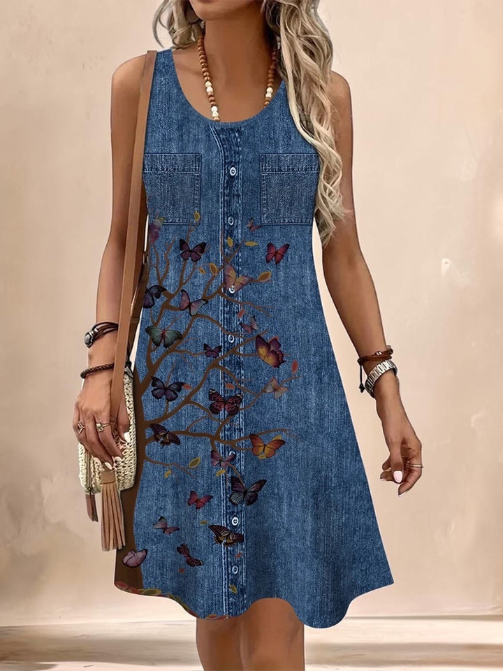 Vivian &amp; Cole Marguerite sleeveless denim-style dress with a butterfly and tree print, round neckline, and A-line cut.