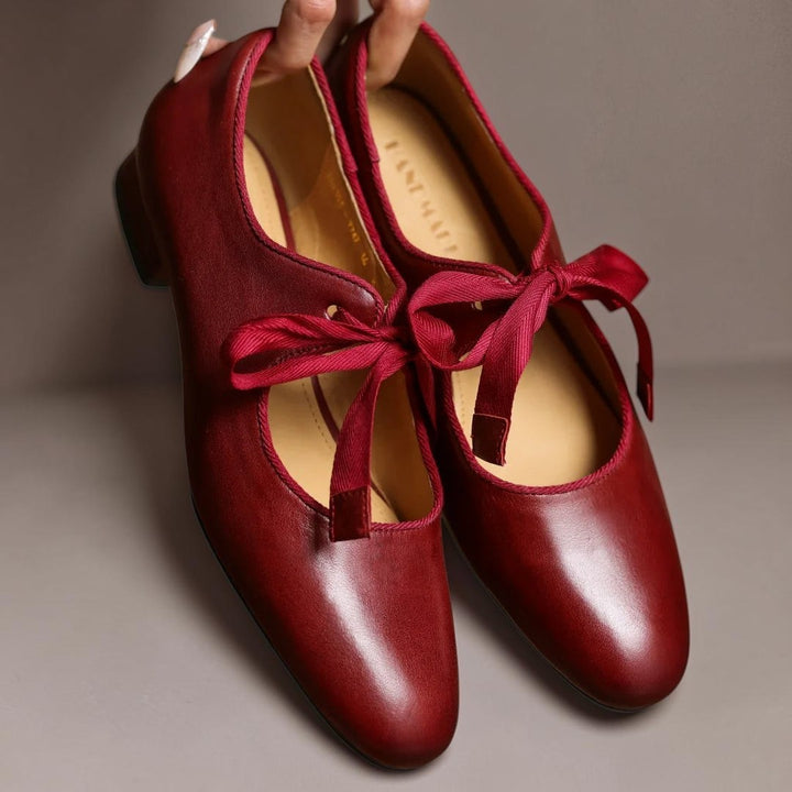 Vivian &amp; Cole Rosamund red leather Mary Jane flats with a delicate ribbon bow detail held by a hand.