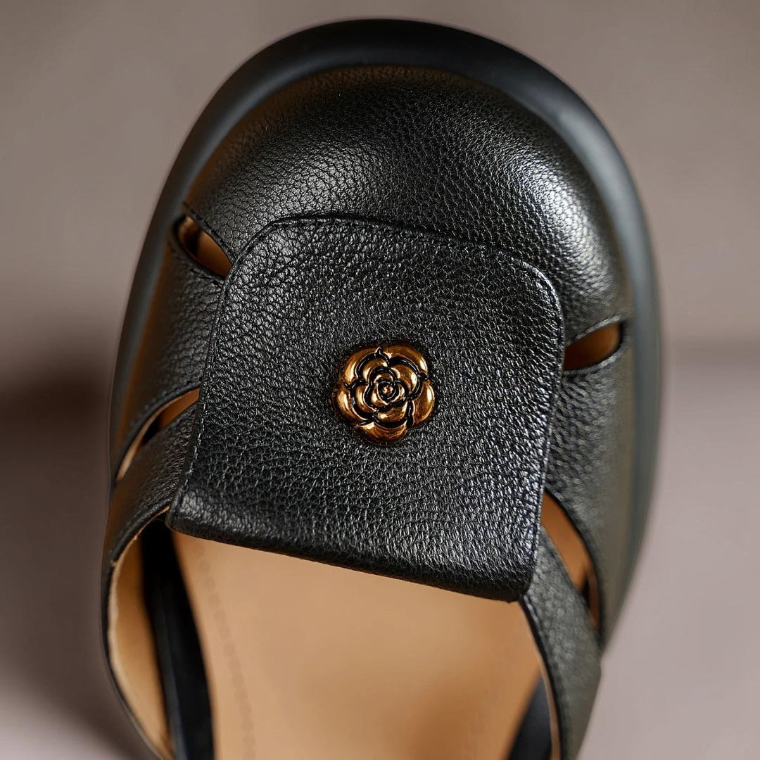Vivian &amp; Cole Seraphine black platform sandal featuring a textured leather upper and a decorative gold rose emblem.