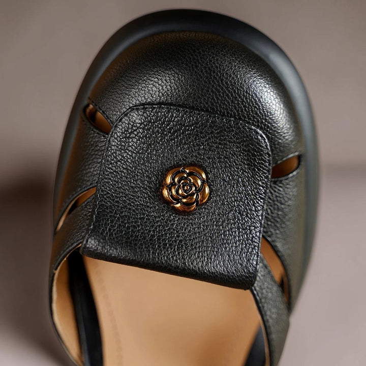 Vivian &amp; Cole Seraphine black platform sandal featuring a textured leather upper and a decorative gold rose emblem.